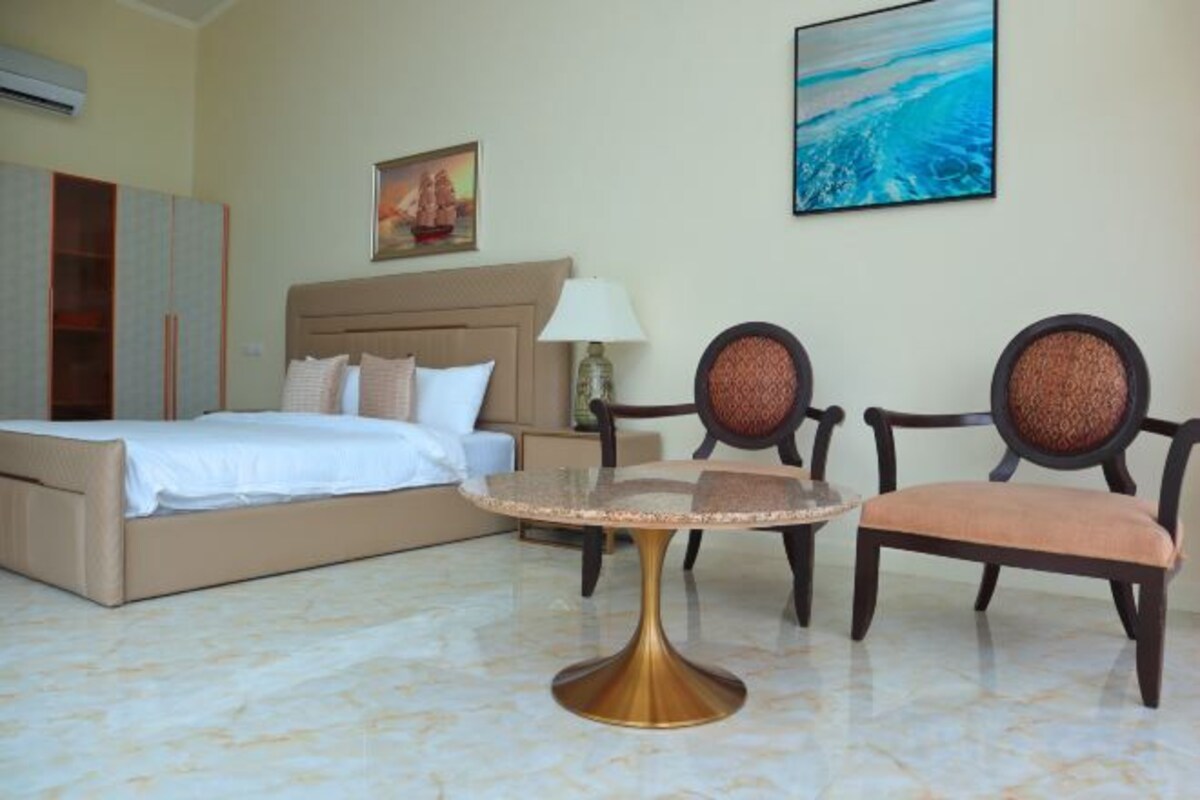 Una camera d'hotel con un letto, due sedie, un tavolino e opere d'arte alle pareti.