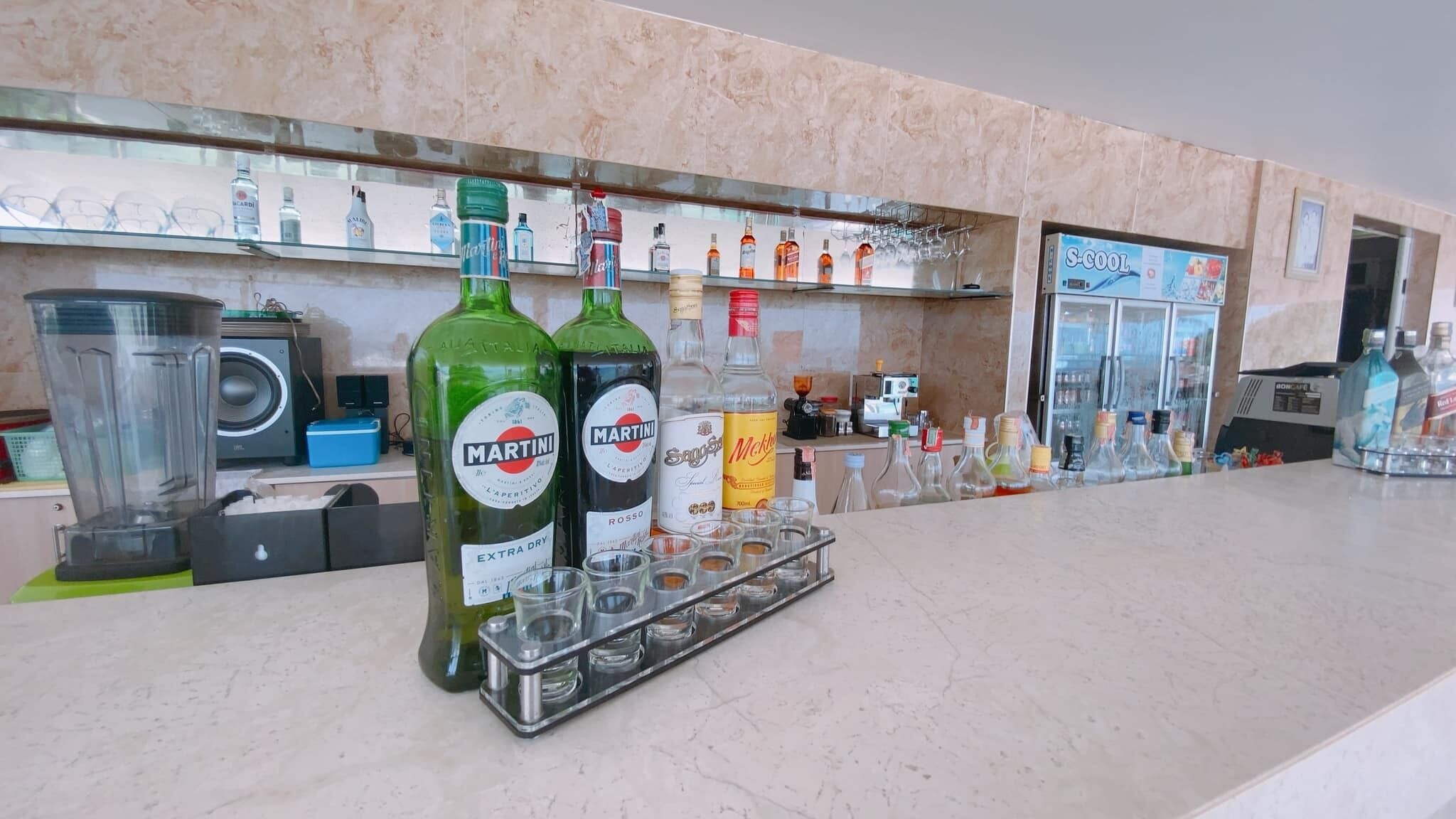 A bar area with Martini and other liquor bottles, a blender, and a S-Cool refrigerator.