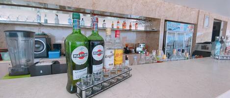 Zona de bar con botellas de Martini y otras licores, una licuadora y un refrigerador S-Cool.