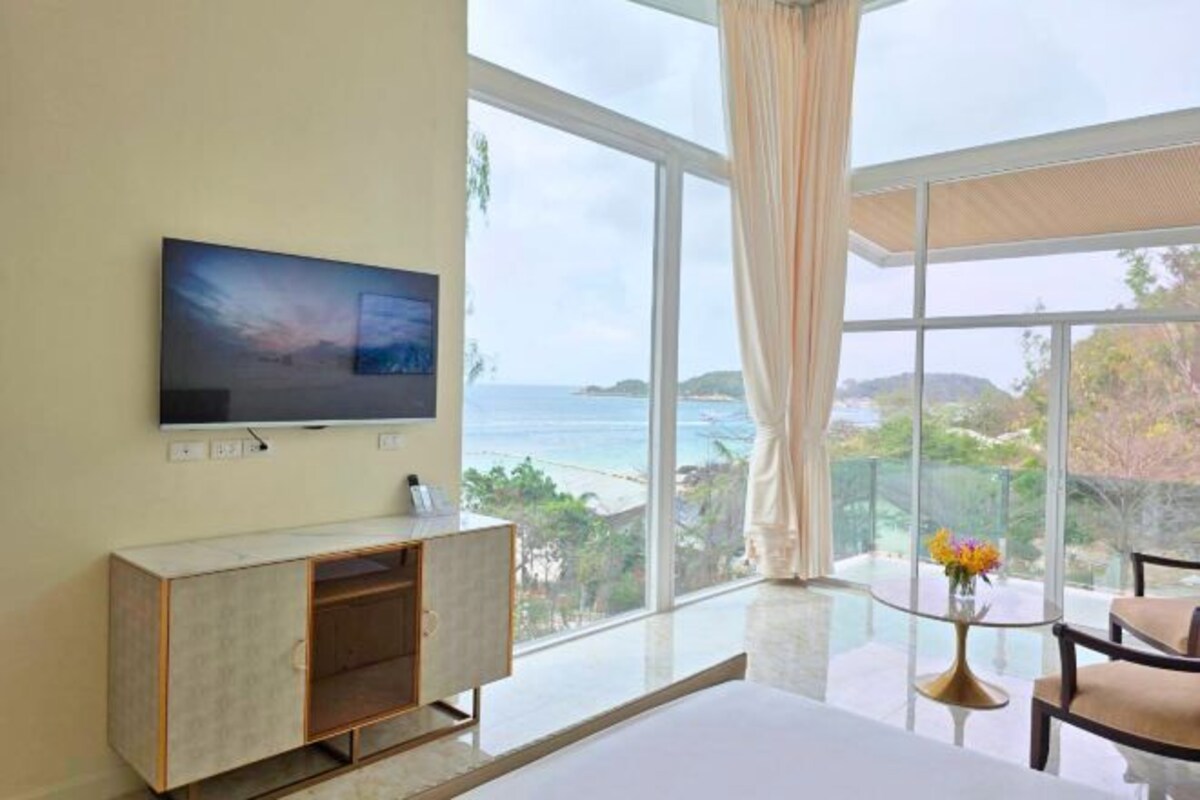 Une chambre d’hôtel dotée d’une grande fenêtre donnant sur la mer et les collines.