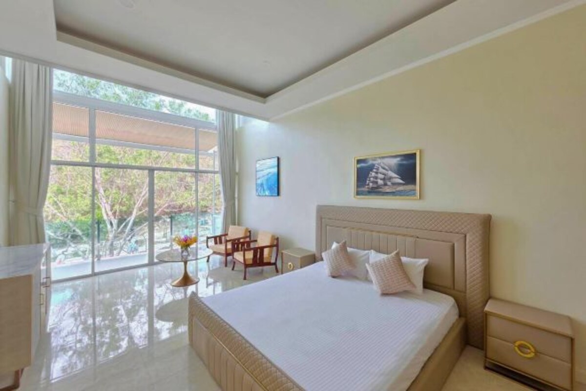 Une chambre spacieuse avec un grand lit, un bureau et une chaise près d’une fenêtre.
