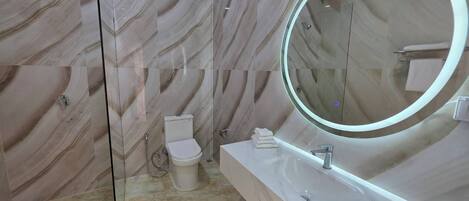 A modern bathroom with a marble wall, a glass-enclosed shower, a toilet, and a vanity with a mirror.