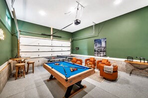 Une table de billard entourée de sièges, un porte-billes et un projecteur fixé au plafond.