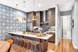 A modern kitchen with a central island, bar stools, and pendant lighting.