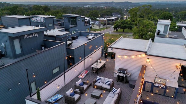 Eine Dachterrasse mit Sitzgelegenheiten im Freien, einem Grill und Lichterketten.