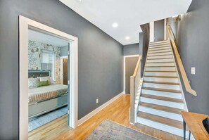 A modern bedroom with a glass door leading to a bathroom, a wooden staircase, and a patterned rug on the floor.