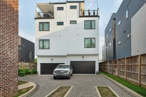 En moderne boligbygning med flere etager, hvid facade, to garager og en murstensmur til venstre.