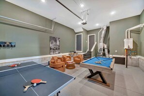 A billiards table with a pool cue and balls, a ping pong table, and a pool table with a blue cloth.