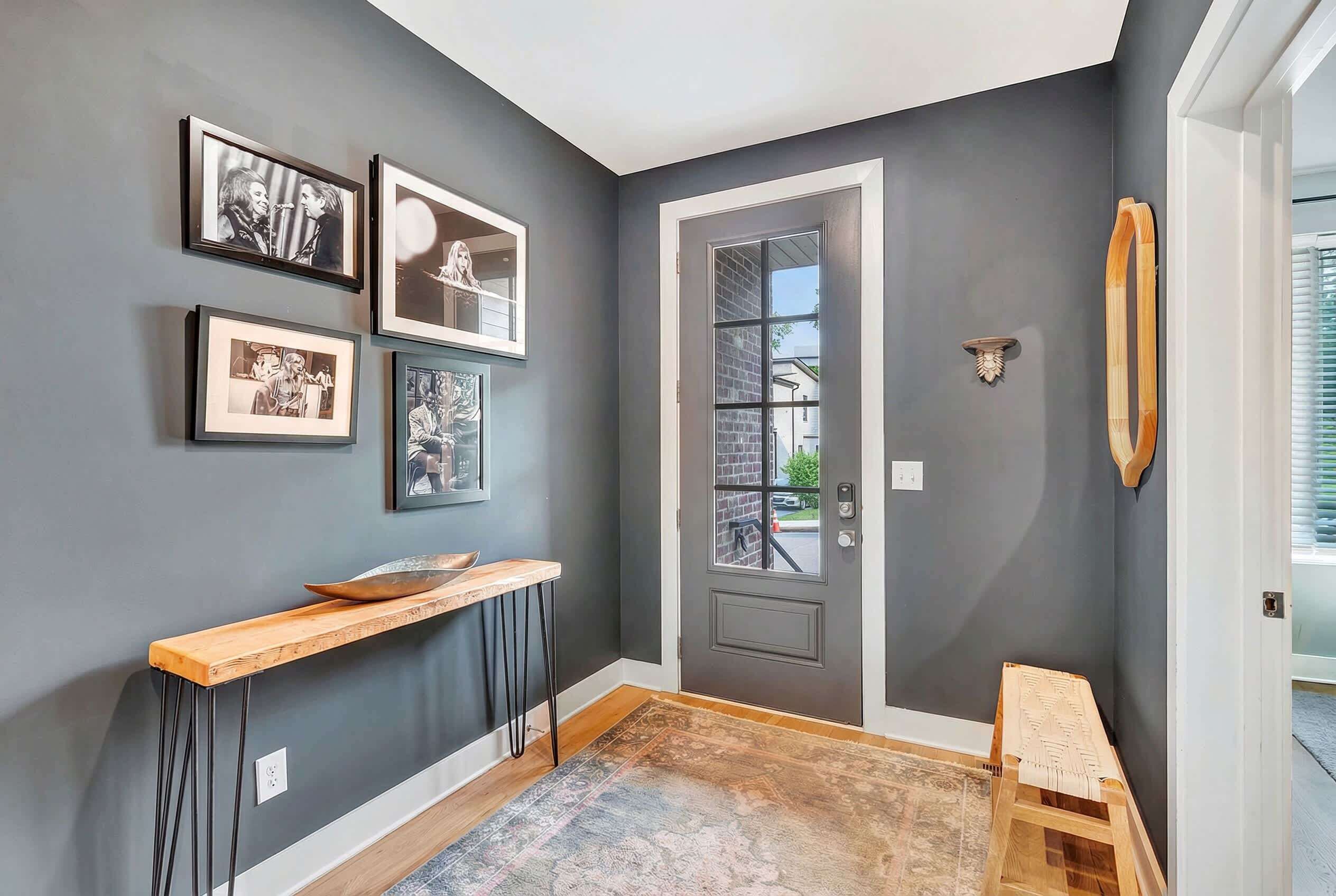 A hallway with a dark gray wall, a wooden bench, a small table, and framed pictures on the wall.