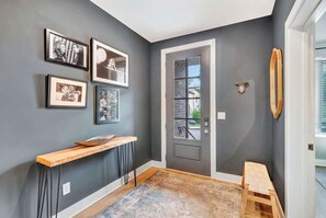 A hallway with a dark gray wall, a wooden bench, a small table, and framed pictures on the wall. - Nashville family getaway: rooftop grill, game room, sleeps 12 (Nashville)
