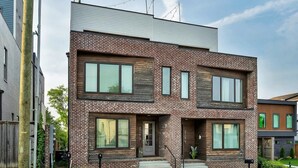 Ein modernes, zweistöckiges Haus mit Ziegelverkleidung, großen Fenstern und einer kleinen Veranda.