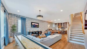 Ein modernes Wohnzimmer mit Billardtisch, einer Couch, einem Fernseher und einer Küche im Hintergrund.