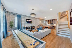A modern living room with a pool table, a sofa, a television, and a kitchen in the background. - Nashville family getaway: rooftop grill, game room, sleeps 12 (Nashville)