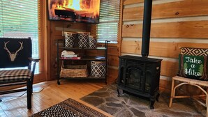 A cozy cabin interior with a fireplace, wooden walls, a bench, and a television displaying a fire. - Harrah`s Casino & Sequoyah National - 6 minutes (Whittier)
