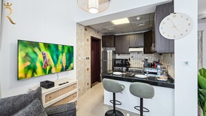A modern kitchen with a TV, bar stools, and a clock. - Peaceful Studio in Prime Al Reem Location (Abu Dhabi)
