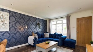 Un salon moderne avec un papier peint à motifs bleus, un canapé bleu, une table basse en bois et une grande fenêtre avec des rideaux.