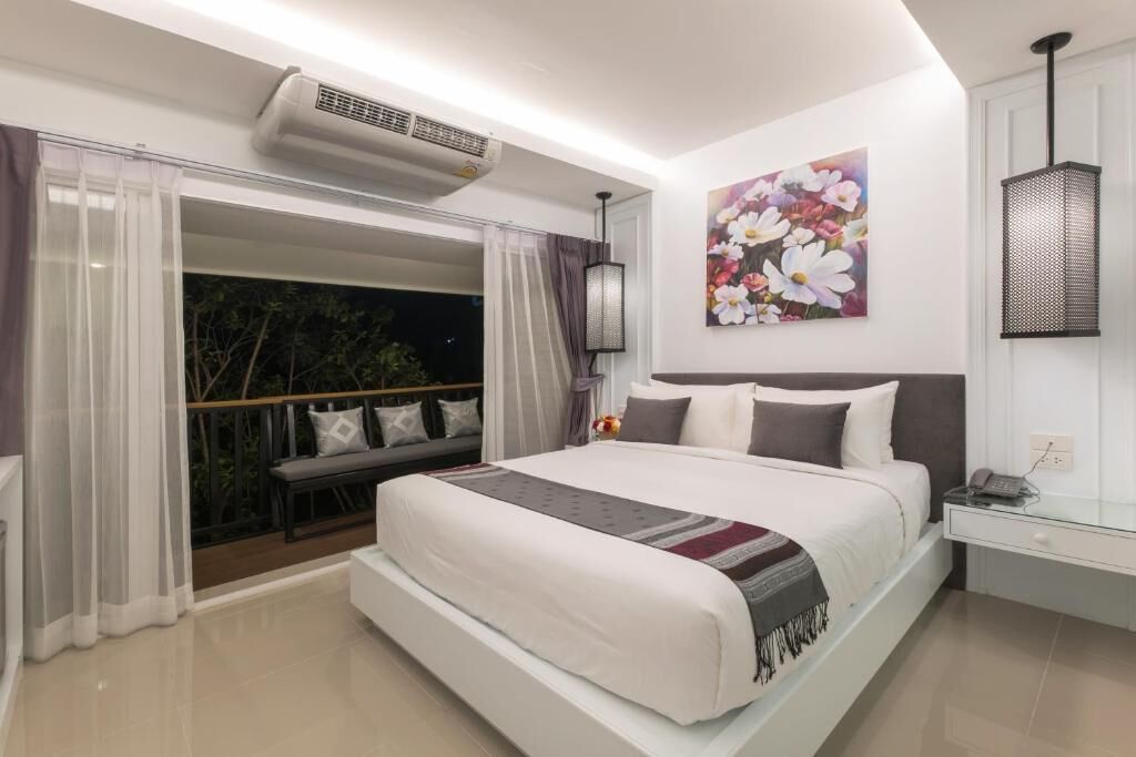 Une chambre à coucher avec un grand lit, une table de chevet, une lampe fixée au mur et une fenêtre avec des rideaux.