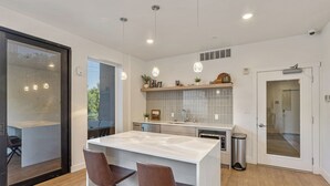 A modern kitchen with a central island, two brown chairs, and pendant lighting.
