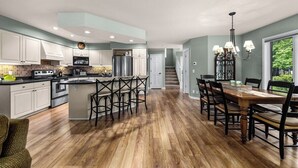 A modern kitchen with a central island, built-in appliances, and a dining area with a wooden table and chairs. - Mountain Harbor Whitefish Captains Quarters 151 (Whitefish)