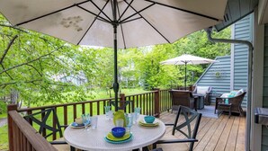 A deck with a round table set for dining, surrounded by chairs, and an umbrella providing shade. - Mountain Harbor Whitefish Captains Quarters 151 (Whitefish)