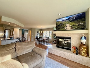 Un salón espacioso con un sofá grande, una chimenea y un televisor montado que muestra un paisaje pintoresco.