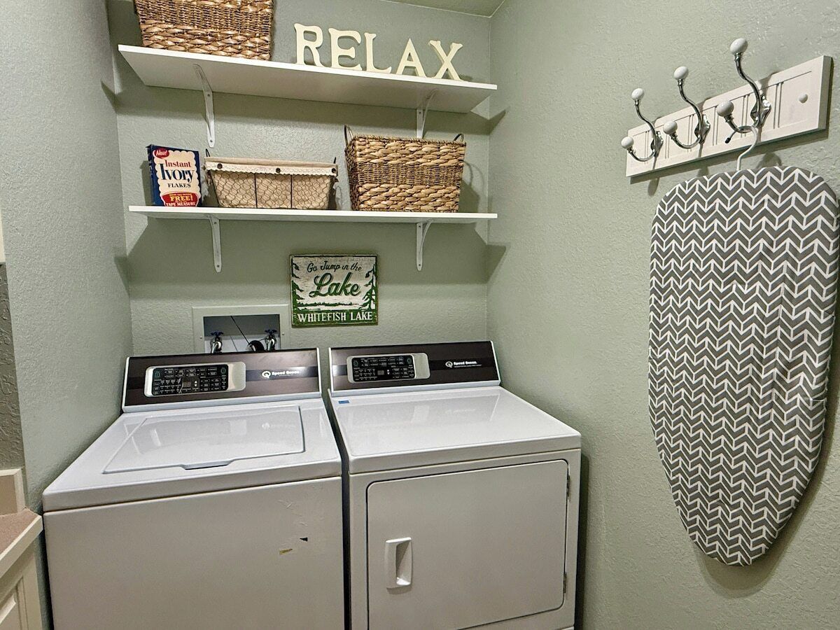 A laundry area with two washers and dryers, shelves with baskets and a sign that says "Go jump in the Lake Whitefish Lake".