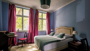 A bedroom with a bed, a desk, a chair, and a window with curtains. - Spend the night in a monument with a view of the trees in the middle of the old town (Halberstadt)