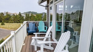 Een houten terras met witte en blauwe Adirondack-stoelen, een glazen deur en uitzicht op het omliggende landschap.