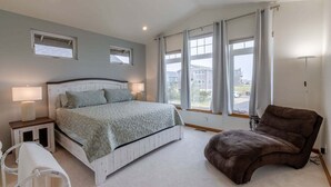 Een slaapkamer met een bed, nachtkastjes, een stoel en grote ramen.