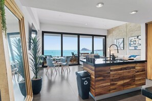 Une cuisine moderne dotée d’un grand îlot central, d’un coin repas avec des chaises et d’une vue sur la mer.