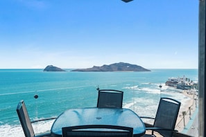 Un balcón con mesa y sillas que da a una playa y al océano.