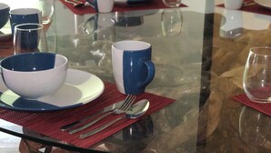 Une table à manger avec un plateau en verre, entourée de chaises en bois et agrémentée d’un pilier central en bois.