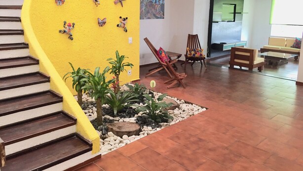 Un escalier avec un mur jaune, des décorations murales représentant des papillons, une chaise en bois, une table basse en verre et un coin salon avec un canapé et des coussins.