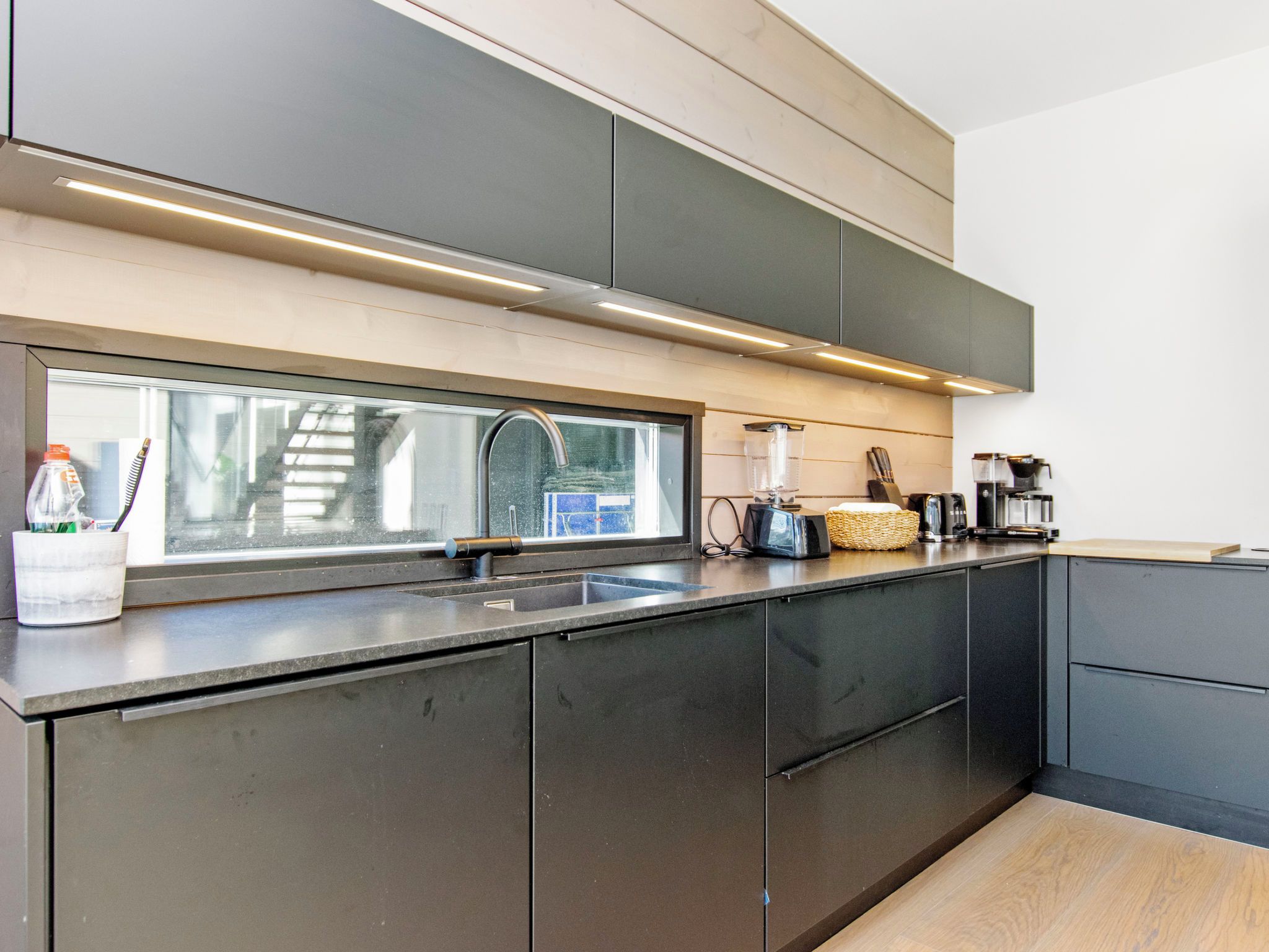 A modern kitchen with a large window, stainless steel appliances, and a wooden countertop.
