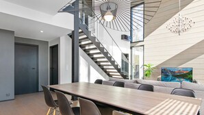 A modern dining area with a long table, chairs, and a staircase.