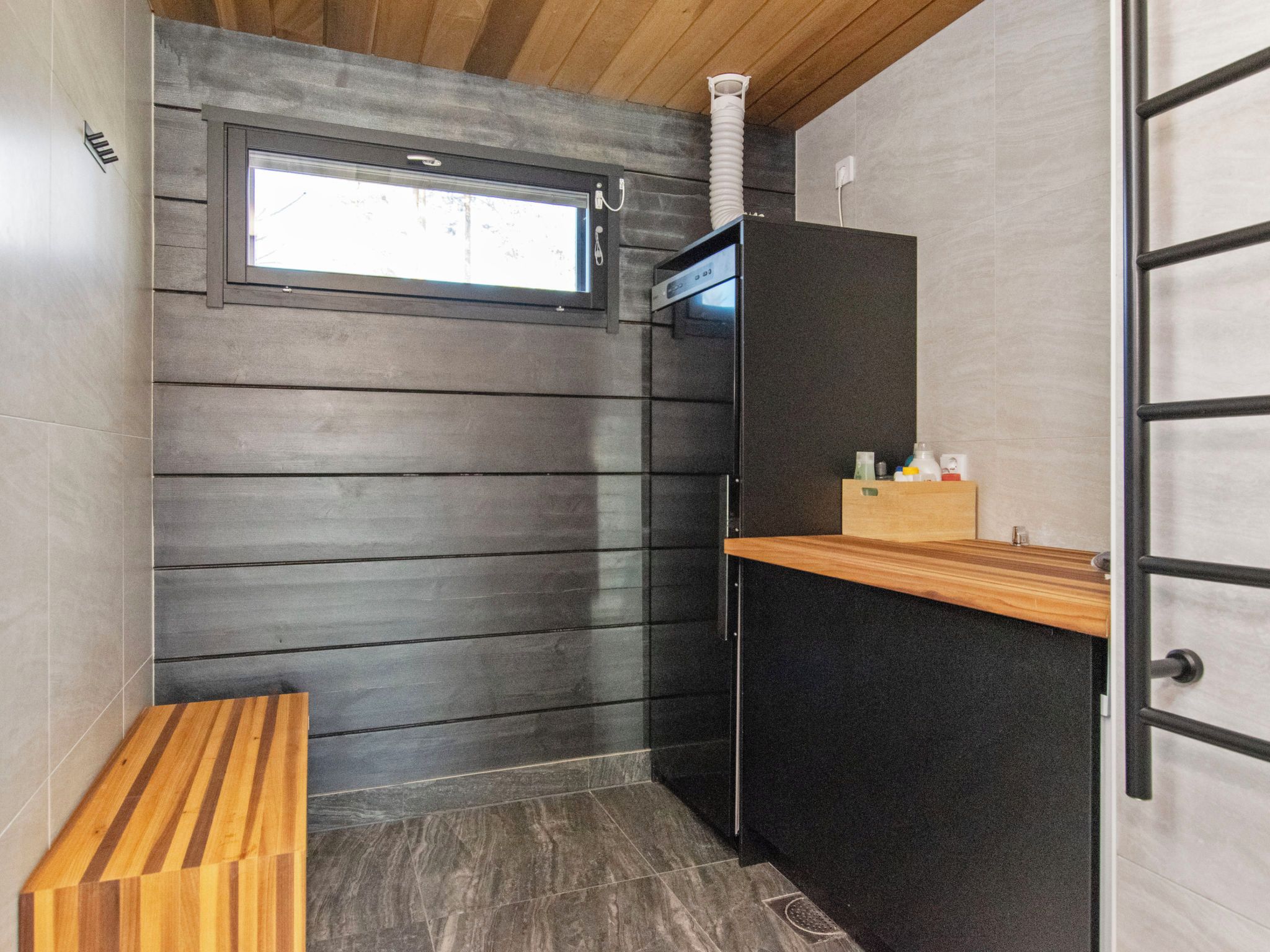 Un baño pequeño con un banco de madera, una ventana y un lavabo con artículos de aseo.