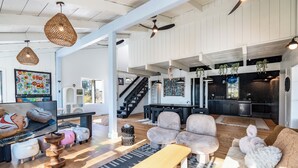 Amplia sala de estar con televisor grande, asientos cómodos, una escalera y una zona de cocina.