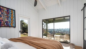 Un dormitorio con una cama grande, vistas a un patio exterior a través de una puerta corrediza de vidrio y un cuadro abstracto colorido en la pared.