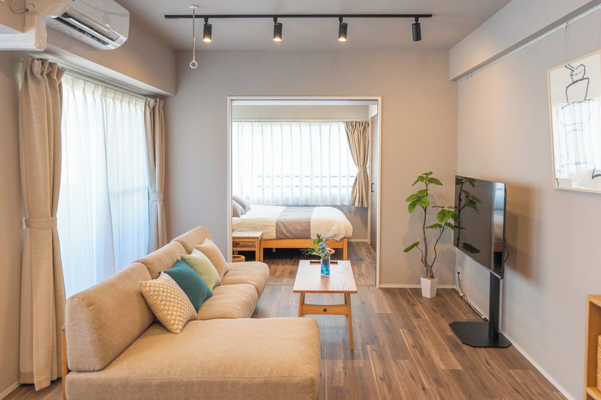 Un salon moderne avec un canapé, une table basse, un téléviseur et un lit à l’arrière-plan.