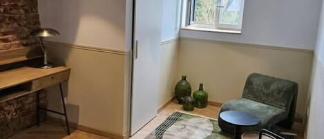 Una sala de estar moderna con piso de madera, un tapete verde estampado, una mesa redonda, un sillón verde y una ventana con vista a follaje.