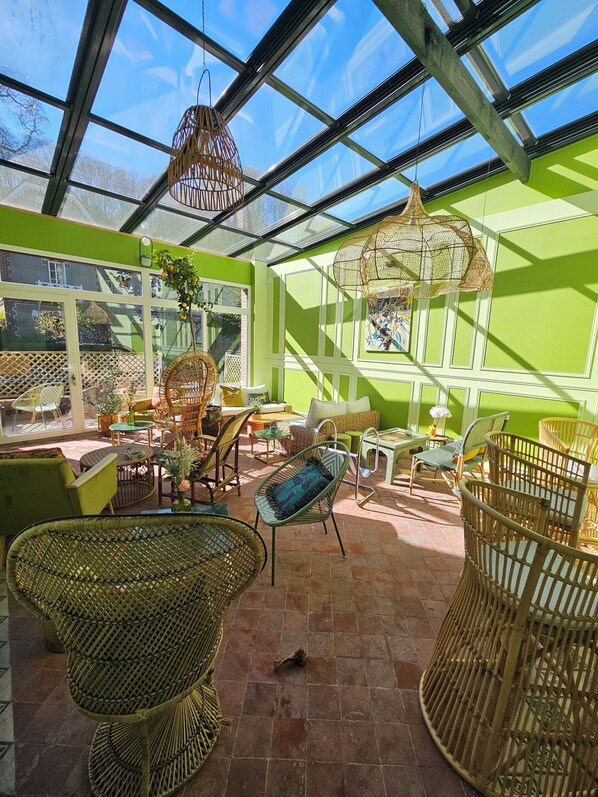 A sunlit room with wicker furniture, a glass ceiling, and a view of the outside.