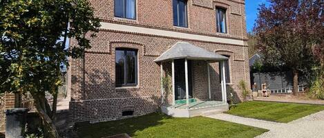 Een tweelaags bakstenen huis met een overdekte veranda en een grindpad.