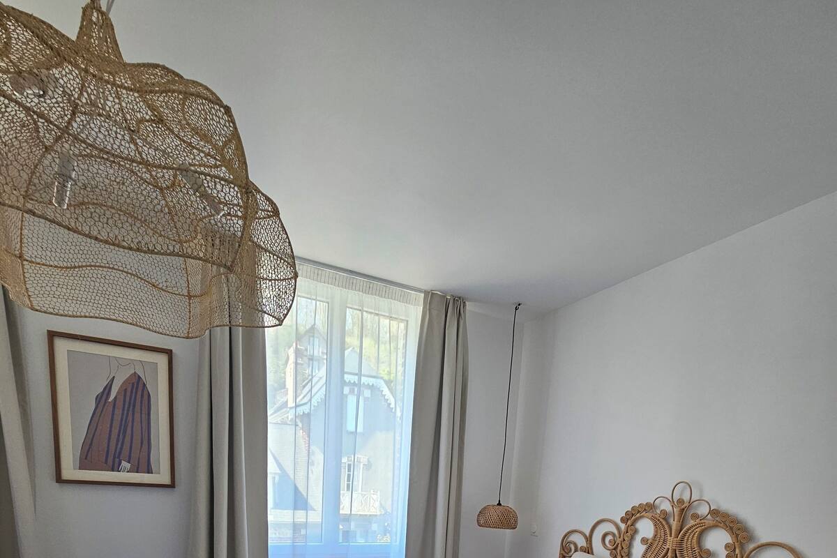 Un dormitorio con una cama grande, un aplique colgante, un radiador y una ventana con cortinas.