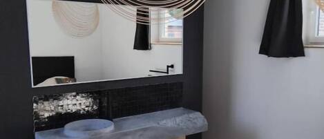 A modern bathroom with a large mirror, a grey sink, and a wooden floor.
