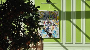 Une pièce avec un mur vert, des meubles en osier, un arbre en pot et un tableau.