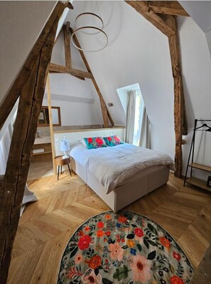 Una camera da letto con soffitto spiovente, travi in legno, un letto con cuscini colorati, un piccolo comodino e un tappeto rotondo.