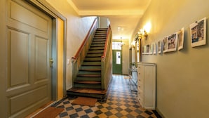 Ein Korridor mit Schachbrettfußboden, einer Treppe mit roter Geländer und einer Tür mit grünem Rahmen.