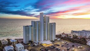 A high-rise hotel with multiple floors and balconies, located near a body of water with a sunset in the background. - One Seagrove Place 1404 (Santa Rosa Beach)