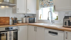 A modern kitchen with white cabinetry, a built-in oven, microwave, and dishwasher. - You will just love the open plan ground floor of this historic cottage. (Flamborough)