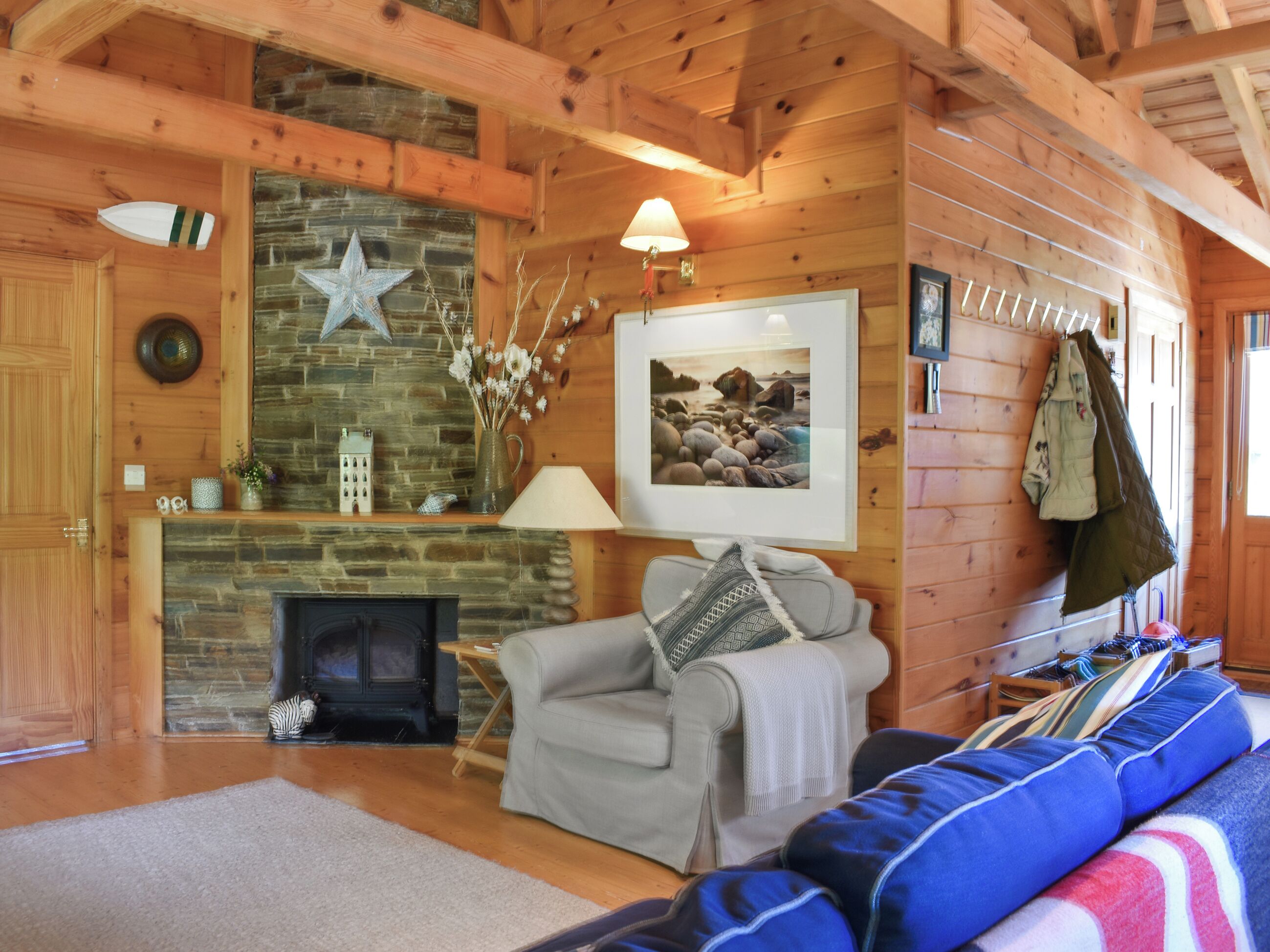 A cozy cabin interior with a stone fireplace, wooden walls, a gray sofa, and a framed picture on the wall.